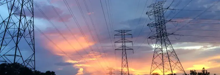 Image of transmission towers against a grey cloudy sky with a yellow sunset at the bottom. Photo by Pok Rie on Pexels